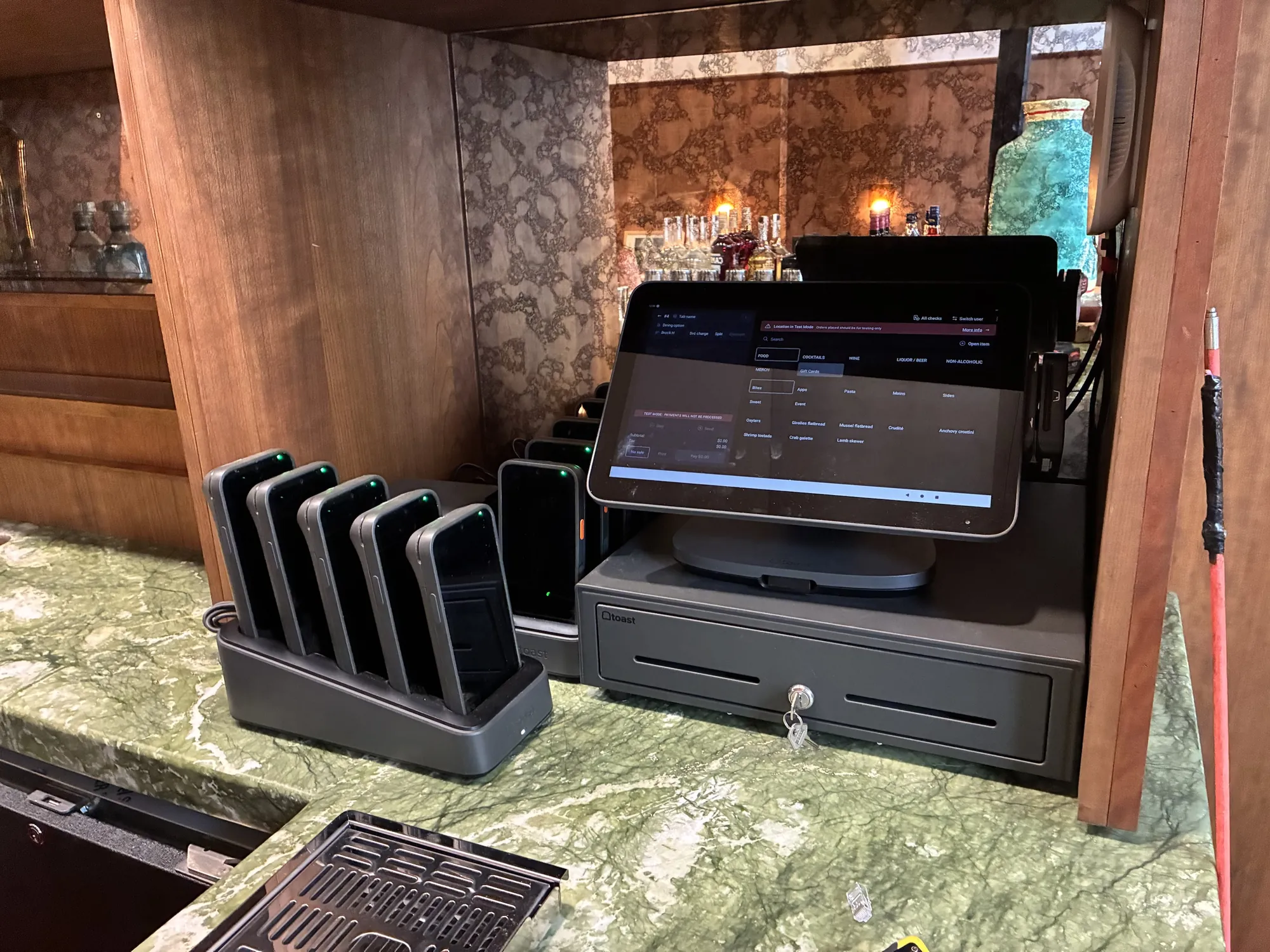 Toast POS terminal, handheld charging dock and cash drawer on the marble bar at Straker's in SoHo