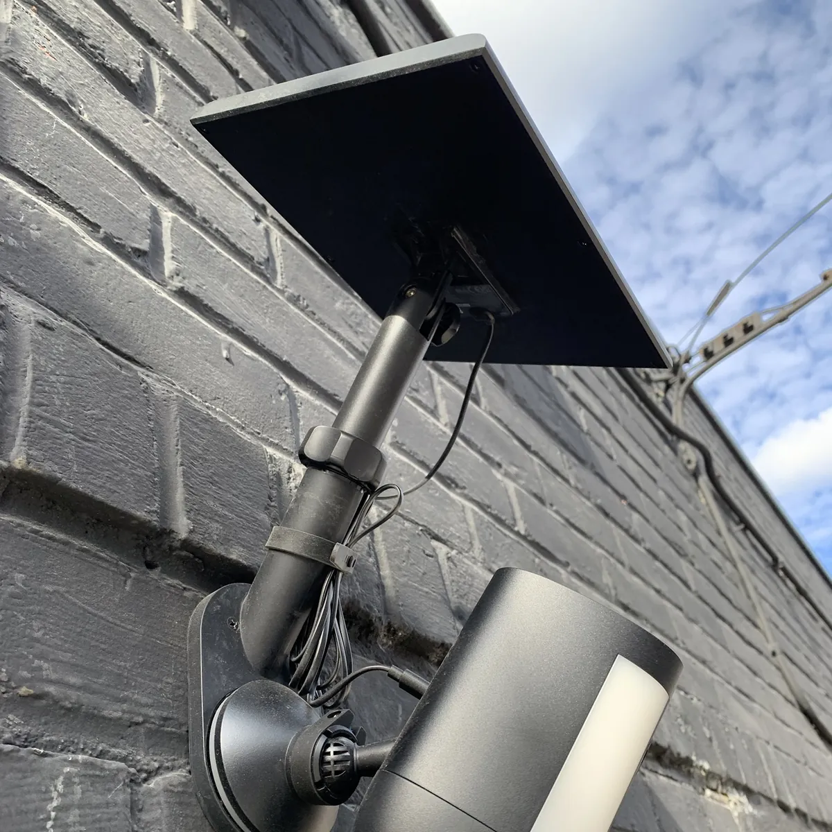Solar-powered spotlight security camera mounted on a painted brick wall