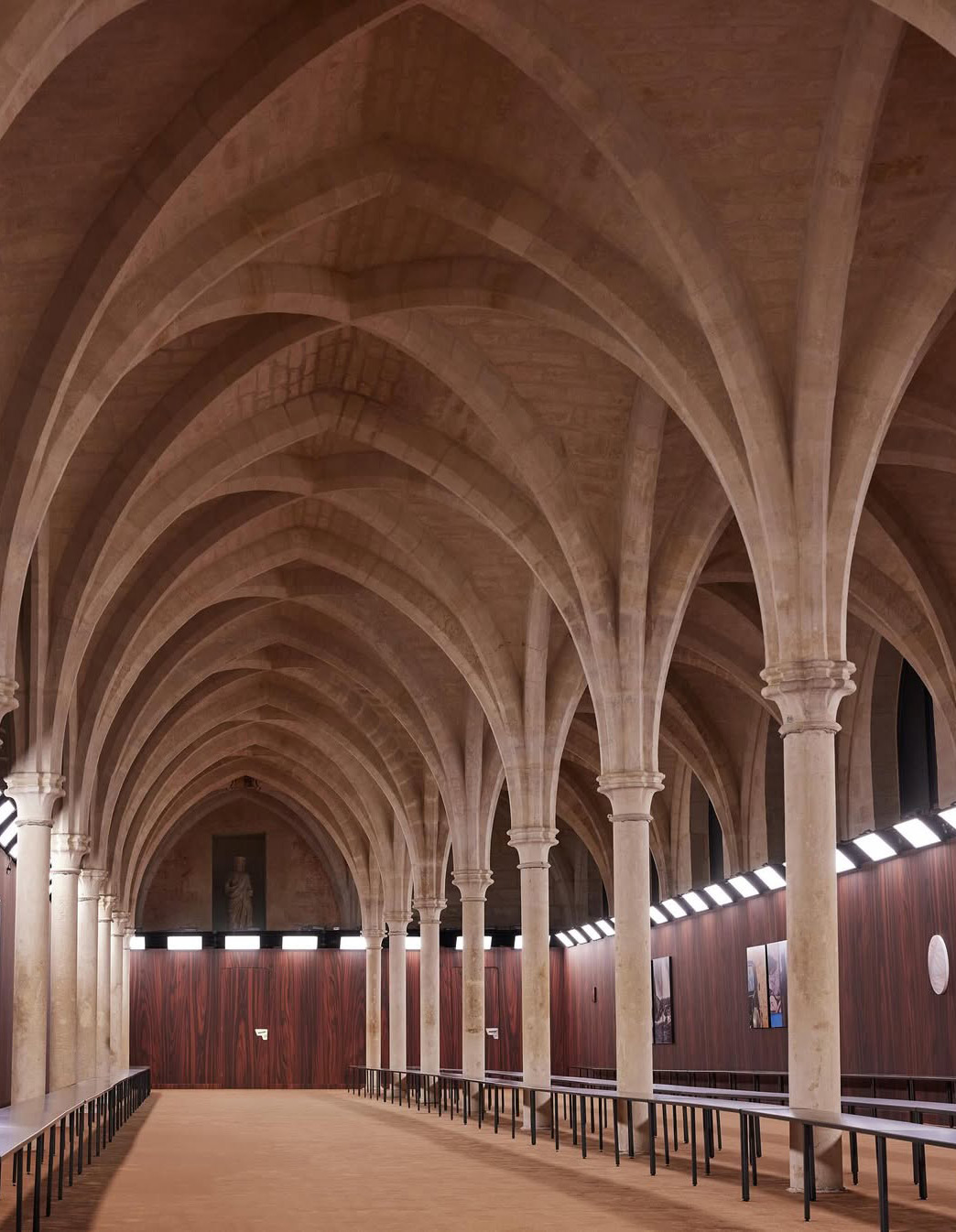 Gothic vaulted hall of the Collège des Bernardins, Paris, with warm wood-effect walls, Acne Studios SS26 show.