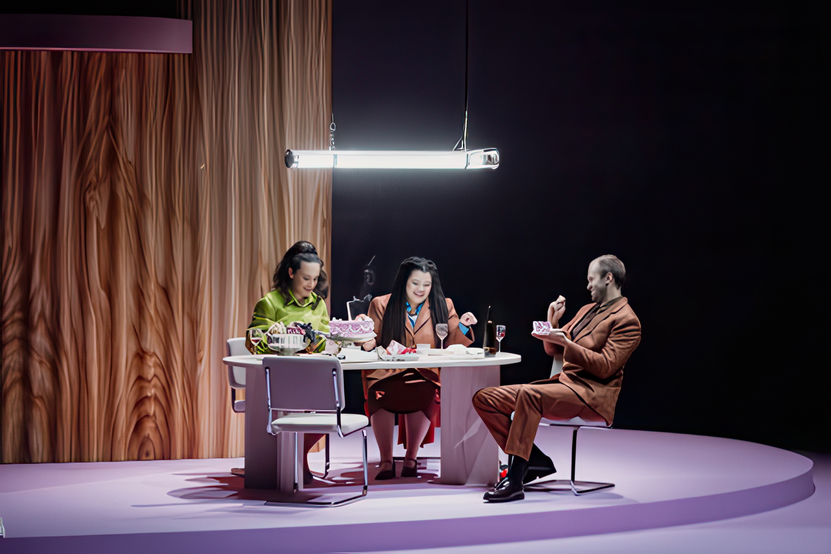 Three singers at a round table on a pale lilac platform in front of a wood-effect wall, Alcina, Opéra de Lille.