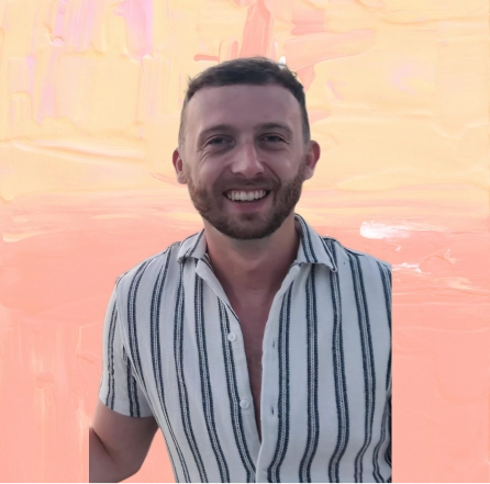 Smiling man with short dark hair and beard wearing a white short-sleeve shirt with vertical black stripes.
