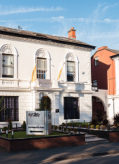 Two-story white building with arched windows, a chimney, and a sign in front that reads 'csm360 Corporate Intelligence' under a clear blue sky.